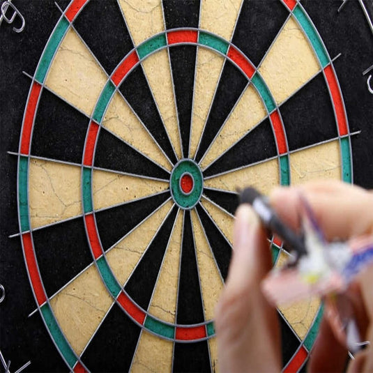 Close-up van een hand die een pijl vasthoudt uit "Perfecte dartpijlen voor beginners en enthousiaste spelers!" 🎯 voor een dartbord met zijn levendige rode, groene, zwarte en beige delen.
