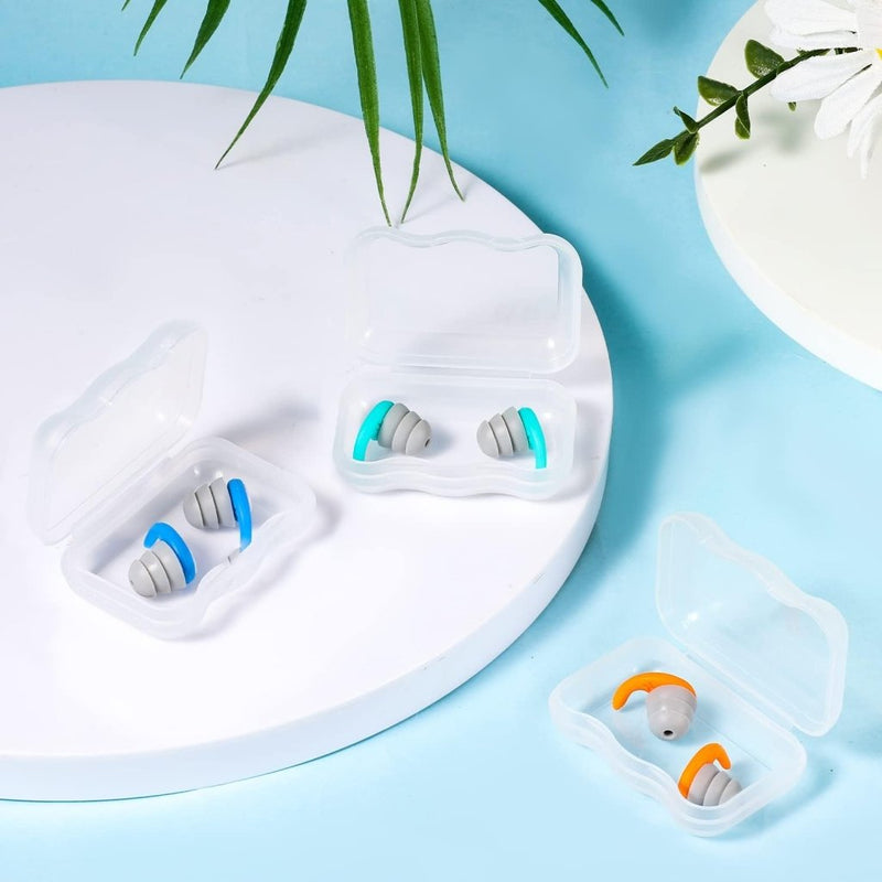 Laad afbeelding in Galerijviewer, Drie paar grijze siliconen zwemoordopjes van Ervaar, met een waterdicht design met blauwe, turquoise en oranje lusjes, zitten in doorzichtige plastic doosjes op een wit en blauw oppervlak, omringd door groene bladeren en een witte bloem.
