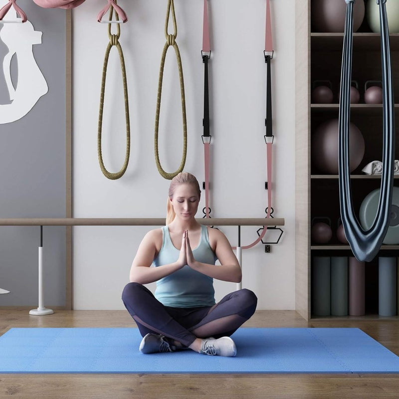 Laad afbeelding in Galerijviewer, Een vrouw zit met gekruiste benen op een Transformeer je vloer met onze zachte interlockende puzzelmat, haar handen in gebedshouding, omringd door fitnessapparatuur en yoga-attributen die de serene sfeer versterken.
