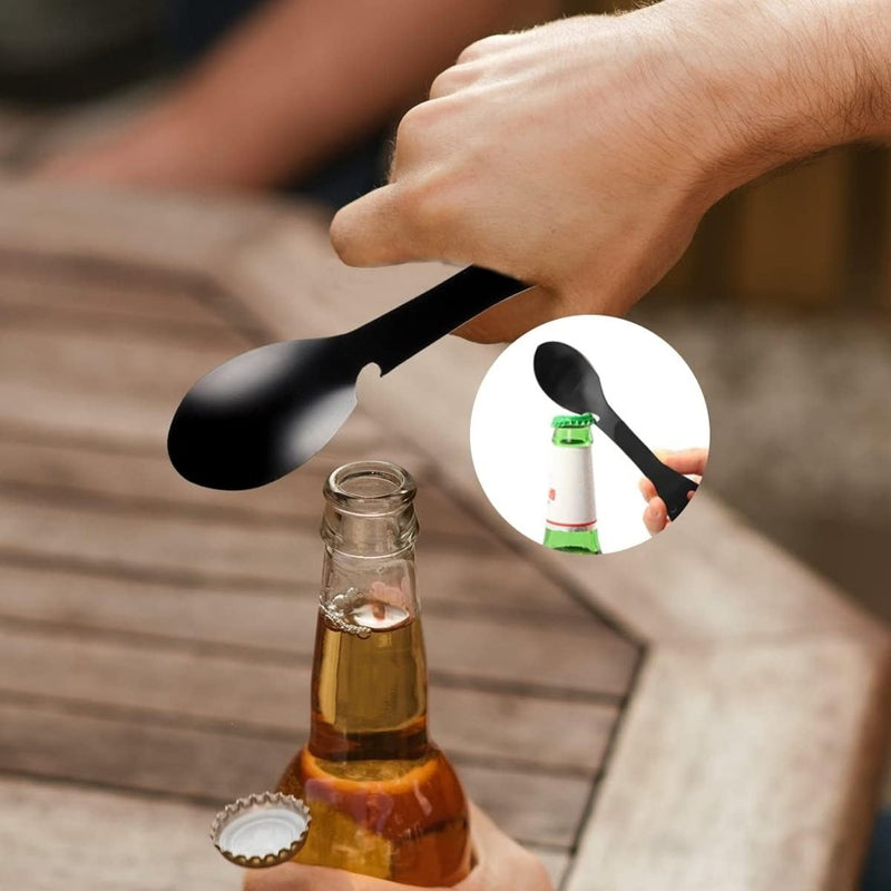 Laad afbeelding in Galerijviewer, Een hand gebruikt &quot;De ultieme multifunctionele camping lepel&quot; om een bruine glazen fles op een houten tafel te openen, gebruikmakend van de ingebouwde flesopenerfunctie.
