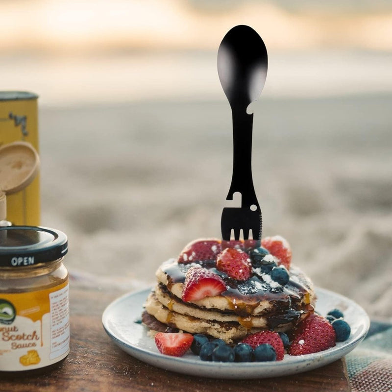 Laad afbeelding in Galerijviewer, Een stapel pannenkoeken met aardbeien en bosbessen wordt elegant versierd met de &quot;De ultieme multifunctionele campinglepel: Jouw beste vriend voor elk avontuur&quot;, geplaatst op een bord naast een pot butterscotchsaus, tegen een serene strandachtergrond.
