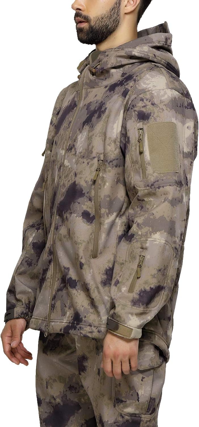 Laad afbeelding in Galerijviewer, Een persoon in een camouflage &quot;Camouflage tactische heren softshell jas: de perfecte metgezel voor je outdoor avonturen&quot; en broek staat zijwaarts met ontspannen handen. De boksjas heeft meerdere zakken met ritssluiting en een capuchon voor extra functionaliteit.
