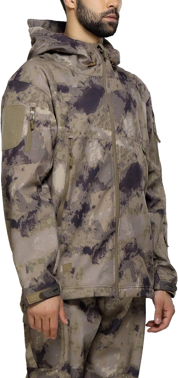 Laad afbeelding in Galerijviewer, Een persoon staat voor een witte achtergrond en draagt de Camouflage tactische heren softshell jas, ideaal voor buitenavonturen, samen met een camouflagebroek met meerdere zakken en een capuchon.

