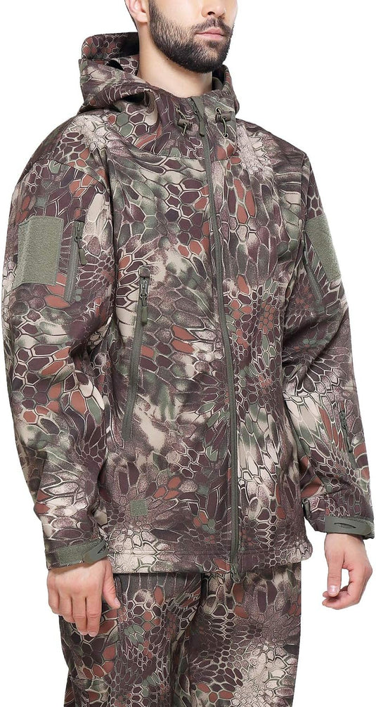 Een persoon staat tegen een witte achtergrond, de handen langs het lichaam, gekleed in een camouflage tactische heren softshell jas: de perfecte metgezel voor je outdoor-avonturen en een bijpassende broek met capuchon.