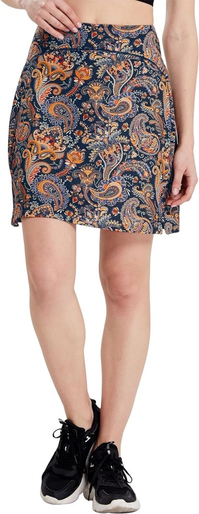 Een persoon in een donkerblauwe 'Sportieve en stijlvolle golfskort voor dames' met paisley-patroon en zwarte sneakers staat tegen een witte achtergrond, wat stijlvolle damessportkleding benadrukt.