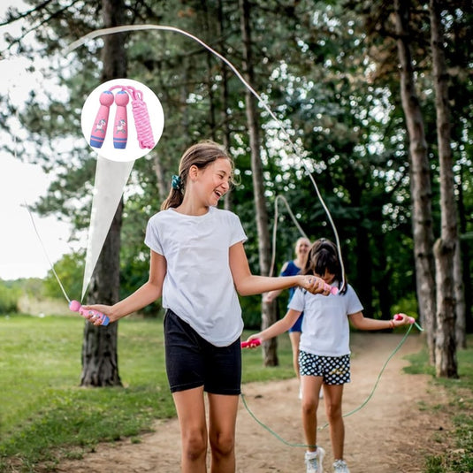 Drie meisjes springen vrolijk touwtjespringen op een bospad, wat de ontwikkeling van het lichaam bevordert. Een close-up benadrukt het roze handvat van het perfecte kinderspringtouw voor eindeloos speelplezier!, wat het plezier vergroot.