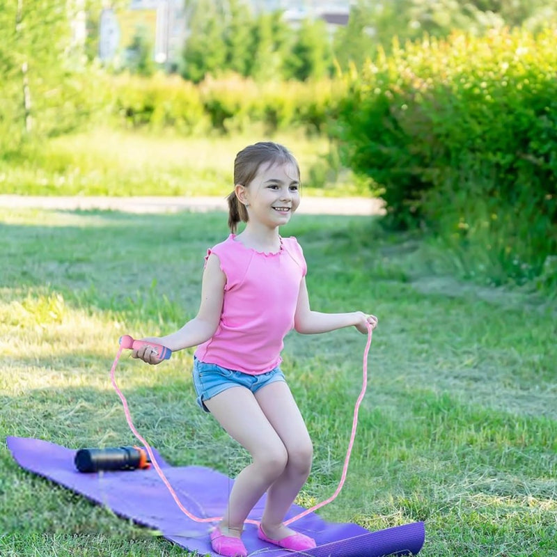 Laad afbeelding in Galerijviewer, Een jong meisje in een roze shirt en korte broek gebruikt &quot;Het perfecte kinderspringtouw voor eindeloos speelplezier!&quot; op een paarse mat buiten in een grasveld, met een bidon in de buurt, genietend van dit moment van lichamelijke ontwikkeling.

