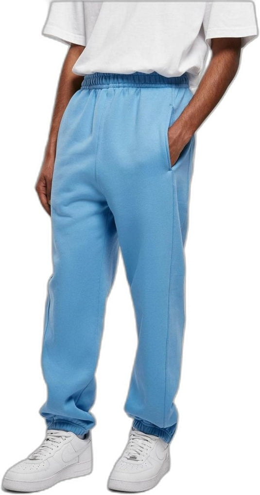 Persoon draagt comfortabele en stijlvolle joggingbroek voor heren in lichtblauw, nonchalant gestyled met handen in de zakken, een wit T-shirt en witte sneakers, staande tegen een effen achtergrond.