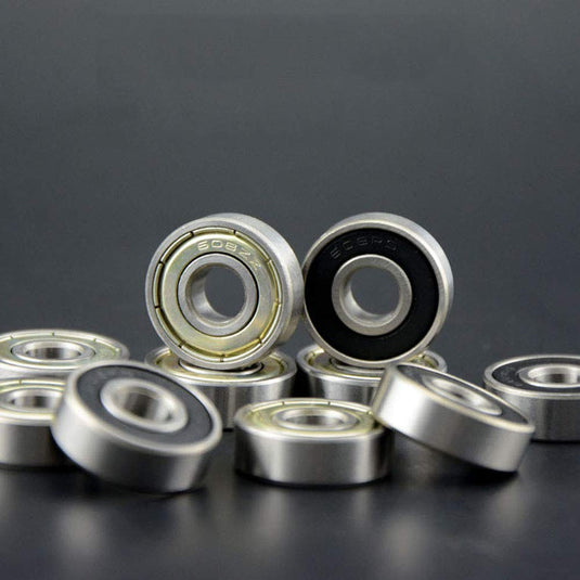 Een close-up van verschillende metalen kogellagers, waaronder koolstofstalen lagers met zwarte binnenringen, rustend op een donkere ondergrond. Deze "Optimaliseer je skateboardprestaties met onze hoogwaardige skateboardlagers - 30 stuks" beloven soepele prestaties met hun strakke metallic afwerkingen.