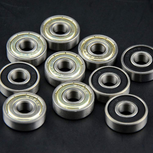 Tien metalen skateboardkogellagers op een donker oppervlak, met verschillende afdichtingen met metalen schilden en zwart rubber voor optimale skateprestaties, afkomstig uit onze hoogwaardige 30-delige lagerset.