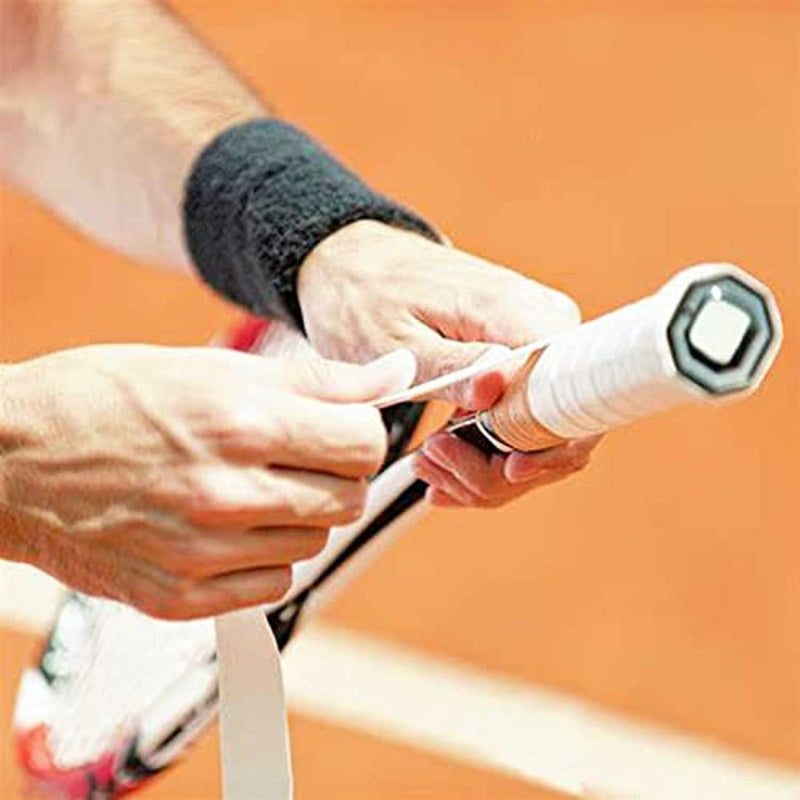Laad afbeelding in Galerijviewer, Op een oranje gravelbaan wikkelt iemand nauwkeurig &quot;Padel grip set: personaliseer je racket en verbeter je spel&quot;-tape rond het handvat van een tennisracket voor een betere grip bij elke slag.
