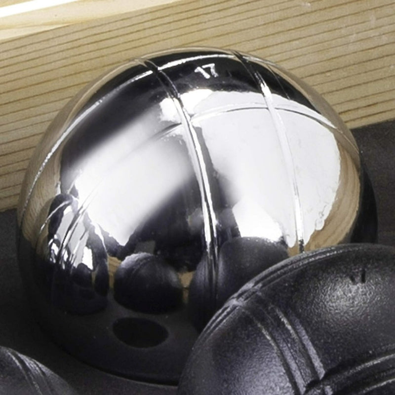Laad afbeelding in Galerijviewer, Op een donker oppervlak ligt een glimmende metalen petanquebal met gegraveerde lijnen, behorend bij het spel &quot;Ervaar petanque plezier met ons prachtige petanque spel in kist van hout&quot;, terwijl andere ballen gedeeltelijk zichtbaar zijn op de voorgrond.
