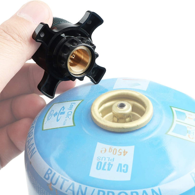 Laad afbeelding in Galerijviewer, Een persoon houdt een zwarte Campingaz-adapter vast naast een blauwe butaangasfles, ter voorbereiding op het aansluiten van de adapter voor het koken tijdens zijn kampeeravontuur.
