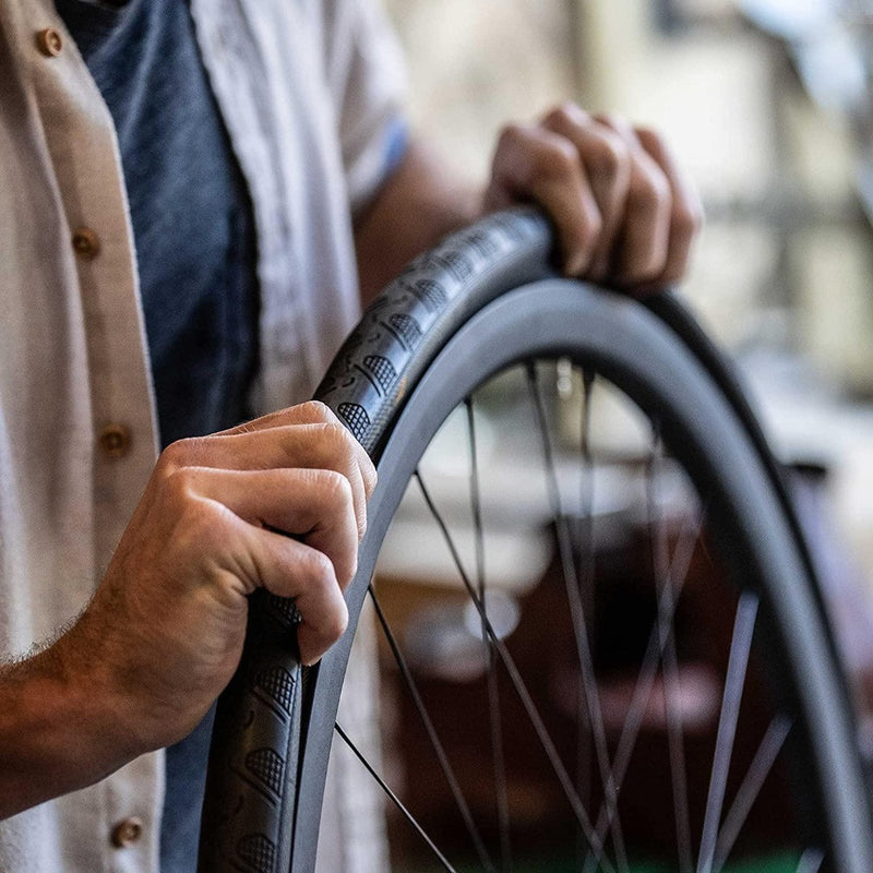 Laad afbeelding in Galerijviewer, Een persoon in een grijs overhemd en een licht overhemd gebruikt vakkundig onze bandentang voor fietsen, &quot;Maak het wisselen van banden eenvoudig&quot;, om een band op een fietswiel te monteren en drukt de rand met gemak over de velg.
