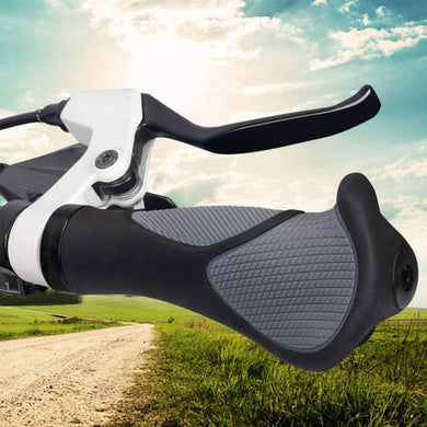 Close-up van een Mtb-handvat met antislip rubberen handvat en remhendel, tegen de achtergrond van een landelijk onverhard pad en groene velden onder een gedeeltelijk bewolkte hemel.