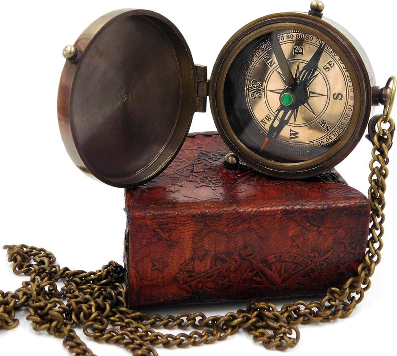 Laad afbeelding in Galerijviewer, Een vintage &quot;Handgemaakt messing zakkompas: een klassieke must-have voor outdoorliefhebbers&quot; met ketting rust op een gesloten, getextureerd bruin lederen boek. Het kompasdeksel is open en geeft nauwkeurige kardinale richtingen en gradenmarkeringen weer.
