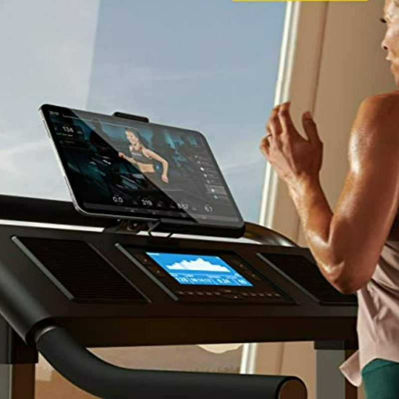 Laad afbeelding in Galerijviewer, Een persoon gebruikt de Loopband en hometrainer tablethouder voor een rustige work-out, waarbij hij of zij op een loopband rent terwijl hij of zij de handen vrij heeft, terwijl hij of zij een video bekijkt op een aangesloten tablet, terwijl het zonlicht door het raam naar binnen schijnt.
