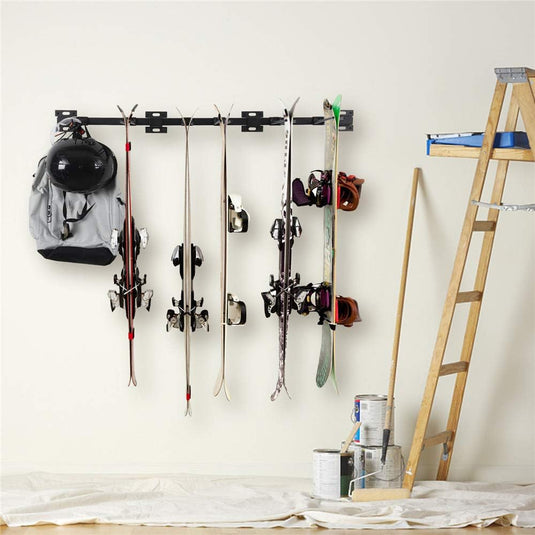 Ski-uitrusting en helm worden netjes opgeborgen op de “Houd je ski's en snowboards veilig en georganiseerd met deze ski en snowboardhouder” van hoogwaardig metaal met afneembare haken, naast een ladder, terwijl verfblikken en een doek verspreid op de vloer liggen.