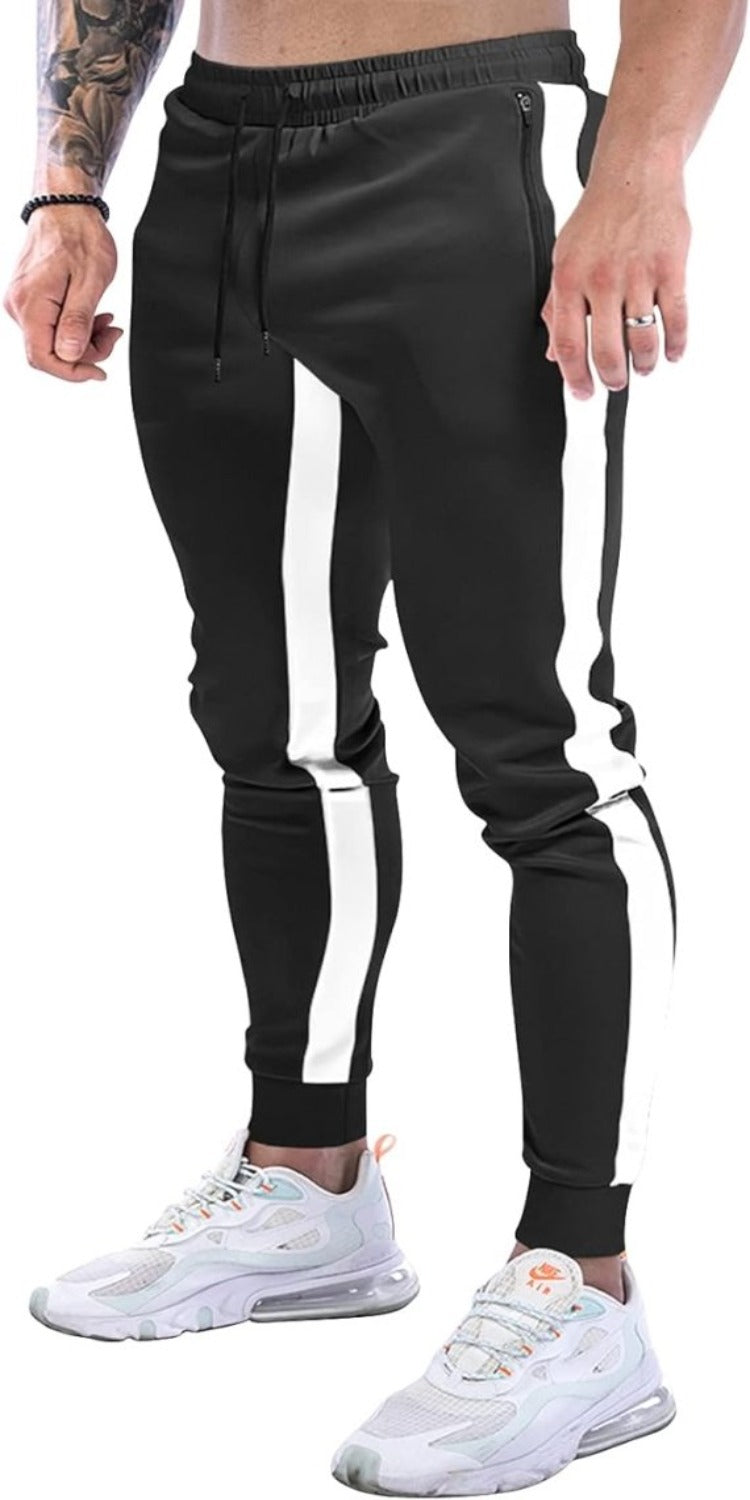Laad afbeelding in Galerijviewer, Een man in een zwarte &quot;Joggingbroek voor heren: comfortabel, comfortabel en stijlvol&quot; met witte zijstrepen en witte sneakers, die in een casual houding een stijlvolle uitstraling uitstralen.
