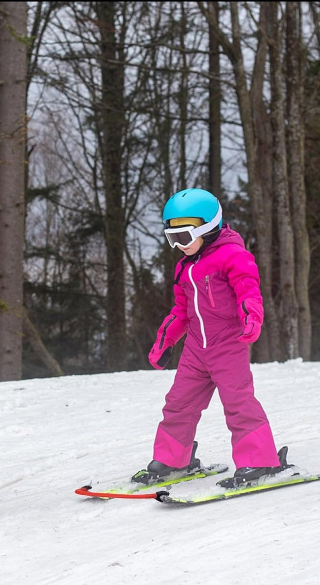 Laad afbeelding in Galerijviewer, Een kind, gekleed in een roze skipak en een blauwe helm, leert veilig skiën op een besneeuwde helling omgeven door bomen. Het is een prachtig voorbeeld van de wonderen van &#39;Leer je kinderen skiën met deze skitipconnector&#39;.
