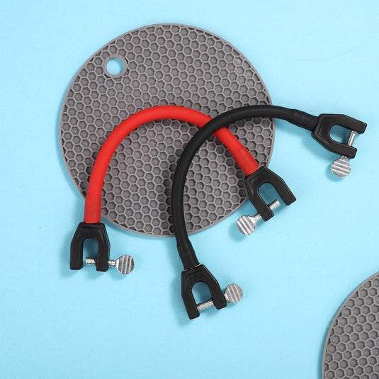 Twee U-vormige spangereedschappen, één rood en één zwart, liggen op een gestructureerde grijze siliconenmat met een honingraatpatroon tegen een lichtblauwe achtergrond. Deze apparaten zijn essentieel voor het gebruik van de "Leer je kinderen skiën met deze skitipconnector", ter promotie van veilig leren skiën voor kinderen.