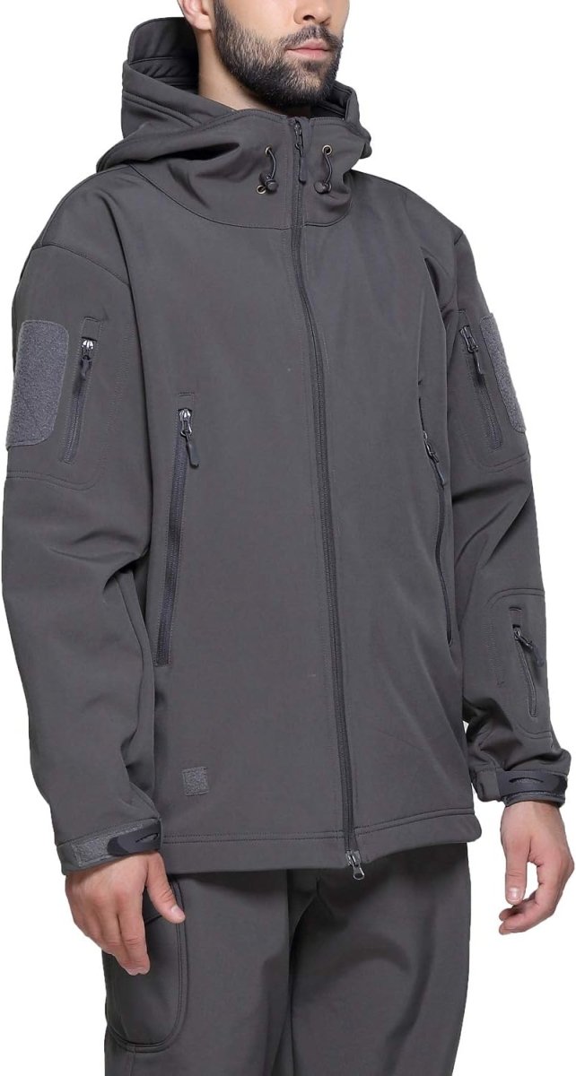 Laad afbeelding in Galerijviewer, Een persoon draagt een grijze Camouflage tactische heren softshell jas met verschillende zakken, ritsen en een capuchon. De jas is waterbestendig en heeft klittenbandpatches op de mouwen. Handen zijn gedeeltelijk zichtbaar.
