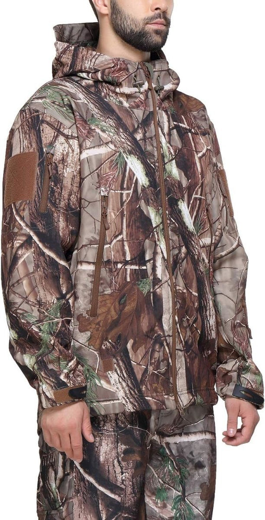 Een persoon die een Camouflage tactische heren softshell jas en bijpassende broek draagt, met een boom- en bladpatroon, straalt zowel stijl als functionaliteit uit voor buitenavonturen.