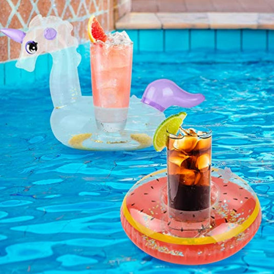 In een zwembad houden twee opblaasbare bekerhouders de drankjes drijvende: een eenhoorn houdt een roze drankje vast met fruitgarnering, en een watermeloenring houdt een donker drankje met een partje limoen vast.