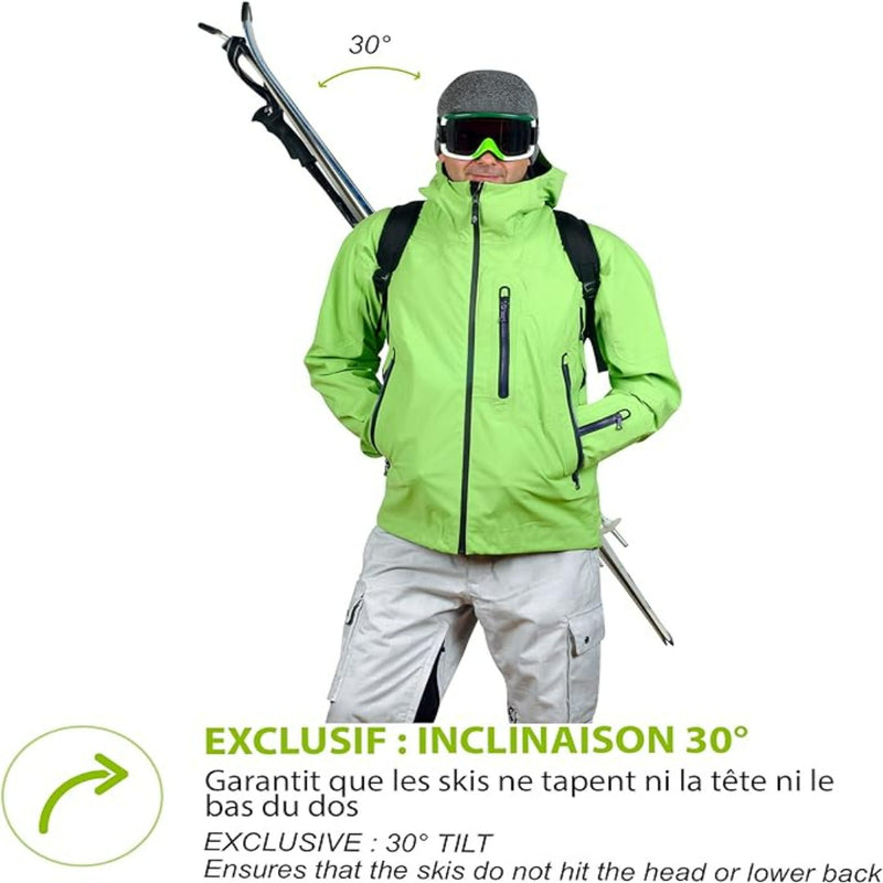 Laad afbeelding in Galerijviewer, Iemand draagt een groene jas en een witte broek en draagt vakkundig de ski&#39;s in een hoek van 30 graden met behulp van de Skiback, zodat hij zijn handen vrij heeft en de ski&#39;s comfortabel kan dragen.
