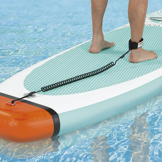 Een beginner staat zelfverzekerd op het Vitamine Sea stand-up paddleboard in een zwembad, met een enkelband stevig vastgemaakt.