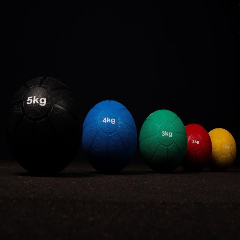 Laad afbeelding in Galerijviewer, Vijf &quot;Train je lichaam met de medicijnbal&quot;-ballen zijn op grootte gerangschikt voor krachttraining: zwart 5 kg, blauw 4 kg, groen 3 kg, rood 2 kg en geel 1 kg. Elke bal rust op een donkere ondergrond.
