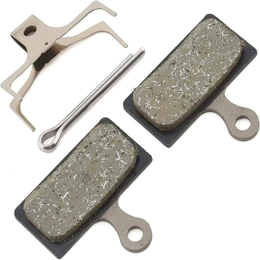 Twee fietsremblokken, een metalen veer en een bevestigingspin worden gepresenteerd op een witte achtergrond, wat het krachtige ontwerp benadrukt. Perfect voor wie compatibiliteit nodig heeft met de G03s remschijf: De ultieme remprestaties voor elke fietser.