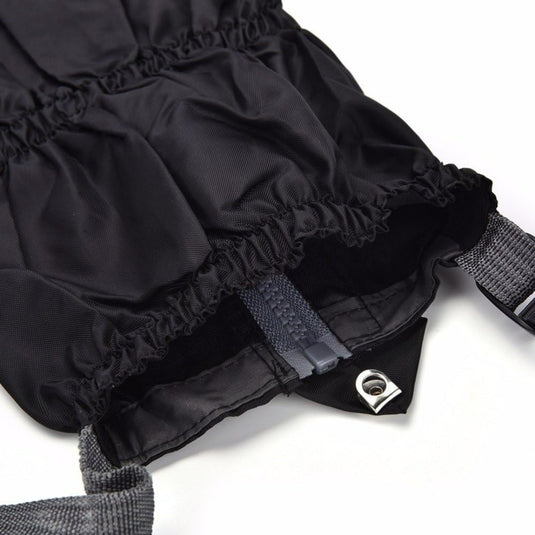 Close-up van een zwarte tas met trekkoord en grijze riemen, ideaal voor buitenactiviteiten, voorzien van een metalen doorvoertule en een binnenrits. Product: Gaiters - de ultieme bescherming voor al je buitenactiviteiten.