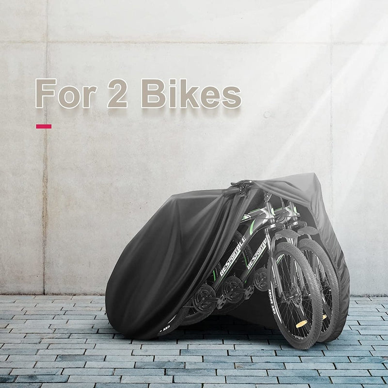 Laad afbeelding in Galerijviewer, Een zwart fietshoes onthult gedeeltelijk twee fietsen op een stenen stoep met een betonnen muur als achtergrond, die bescherming tegen elementen biedt. De tekst luidt: &quot;Bescherm je fiets met onze waterdichte fietshoes voor 2 fietsen.
