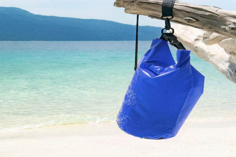 Laad afbeelding in Galerijviewer, Hangend aan drijfhout op een strand met helder water en bergen in de verte, is de &quot;Verken zorgeloos de natuur&quot; blauwe vloeistof tas gemaakt van hoogwaardige materialen voor duurzaamheid.
