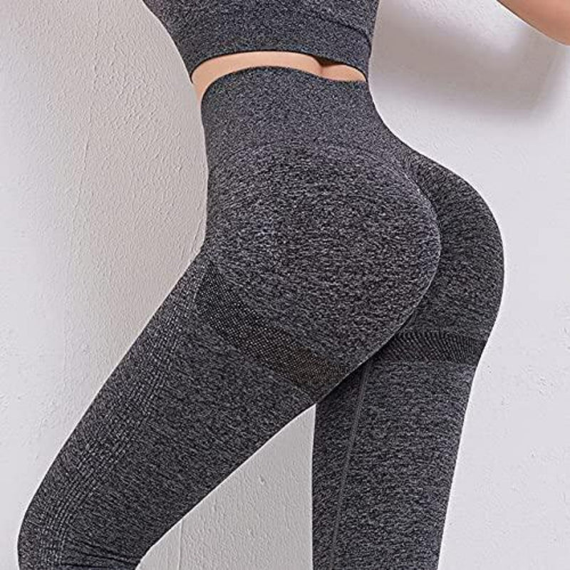 Laad afbeelding in Galerijviewer, Een persoon toont een bijpassend grijs sportpakje, met daarop de zijkant van onze yogaleggings voor dames en een crop top tegen een onberispelijk witte muur.
