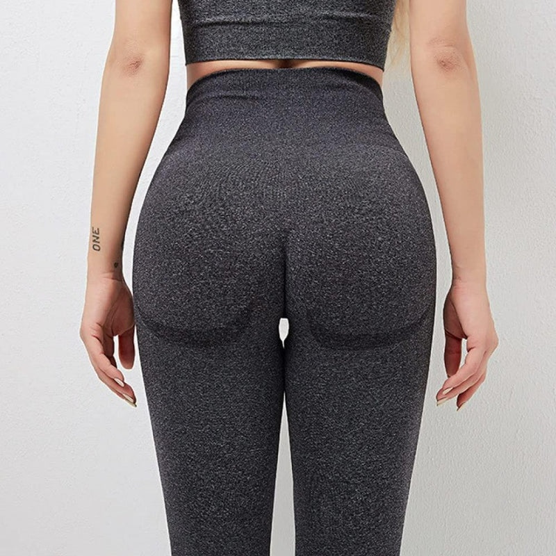 Laad afbeelding in Galerijviewer, Op de achtergrond is een persoon te zien die een nauwsluitende, donkergrijze yogalegging draagt met een hoog getailleerde tailleband, die de perfecte balans biedt tussen stijl en comfort.
