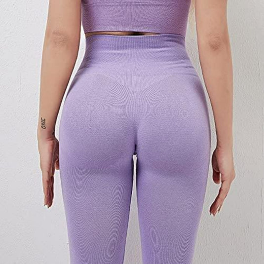 Iemand die een paarse atletiekoutfit draagt, inclusief onze "Ontdek de perfecte balans van stijl en comfort met onze yogaleggings voor dames!" met hoge tailleband, is van achteren tegen een lichte muur gefotografeerd.