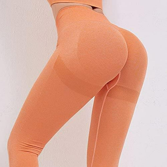 Drager van de Ontdek de perfecte balans van stijl en comfort met onze yogaleggings voor dames! in oranje, met een hoog getaillleerde tailleband en bijpassende crop top, sierlijk poserend tegen een witte achtergrond.