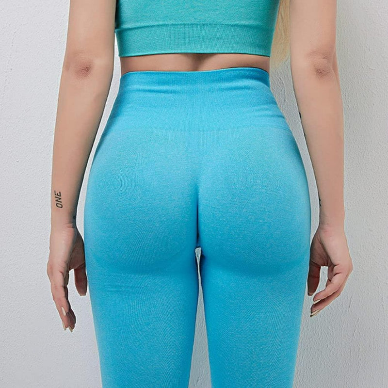 Laad afbeelding in Galerijviewer, Een persoon in een turquoise crop-top en een comfortabele yoga-legging voor dames staat met zijn gezicht naar een muur, met de armen langszij, waardoor een tatoeage op de linkerarm zichtbaar is. Deze yogalegging heeft een hooggetailleerde tailleband en combineert stijl en comfort naadloos: Ontdek de perfecte balans van stijl en comfort!.
