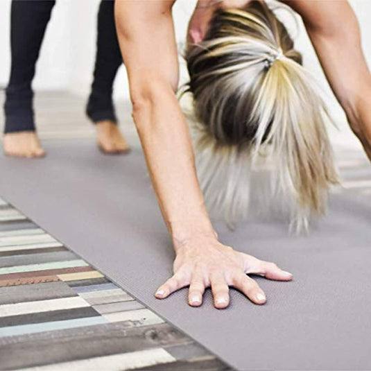 Een persoon met blond haar in een paardenstaart voert de neerwaartse hondhouding binnenshuis uit op de duurzame yogamat - Optimale grip en comfort voor elke yogavorm.