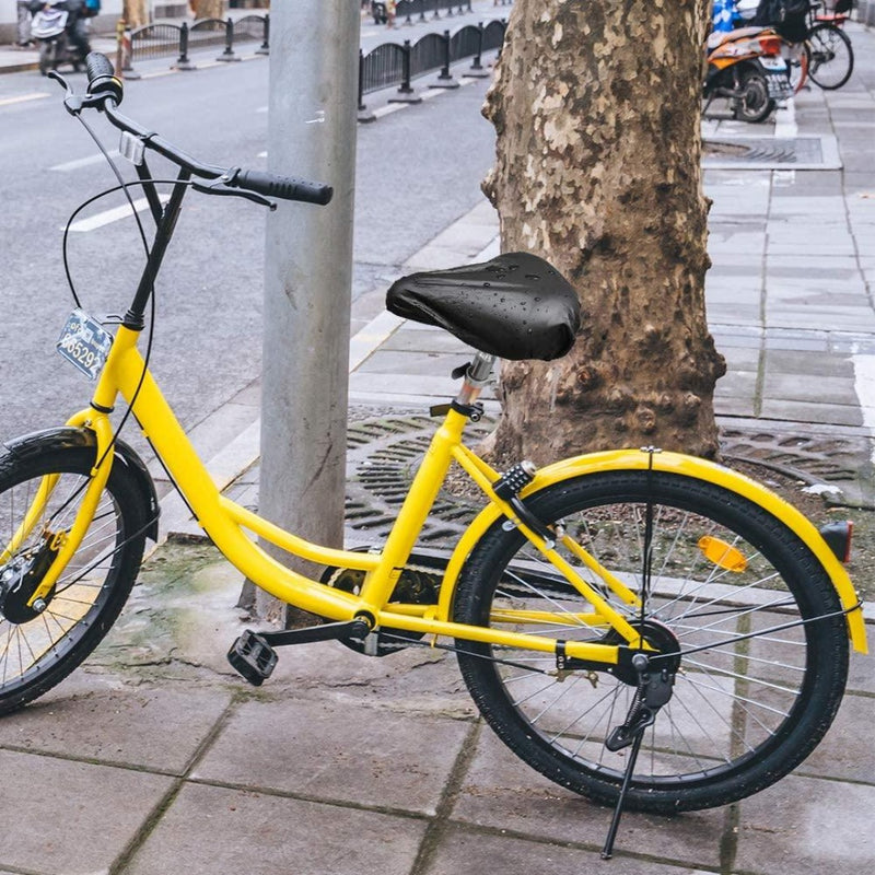 Laad afbeelding in Galerijviewer, Een gele fiets met de Geniet van comfortabele fietsen met onze hoogwaardige zadelhoezen voor optimale bescherming staat geparkeerd op een nat trottoir naast een boom en paal, waarvan de fietszadel lichtjes glinstert.
